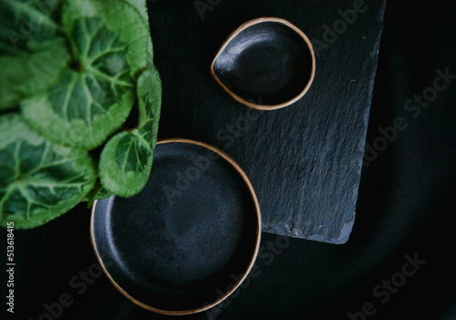 An empty ceramic black plate with gold edging on a black background. Copy of the space view from above - Image