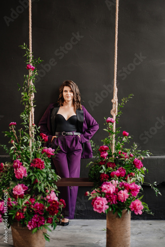 woman in a lilac suit and a sexy black top against a wall in a room with peonies