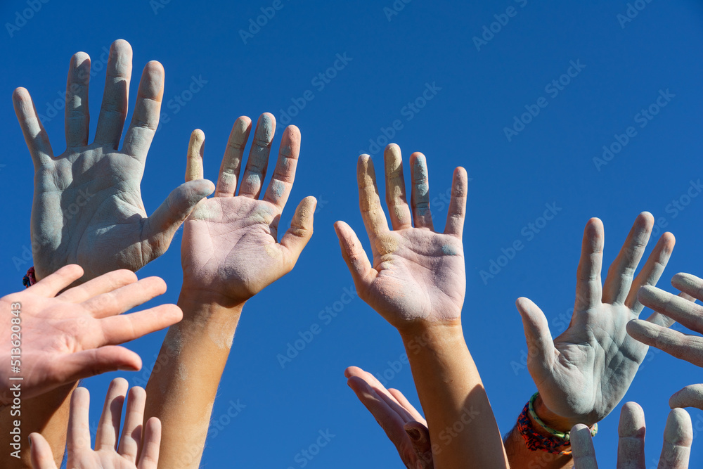 Hands of a group of people with colored chalk powder raised up against the blue sky Hands of a group of people with colored chalk powder raised up against the blue sky