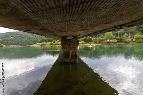 Reflections of the bridge over the river and beside it some canoeists paddle.