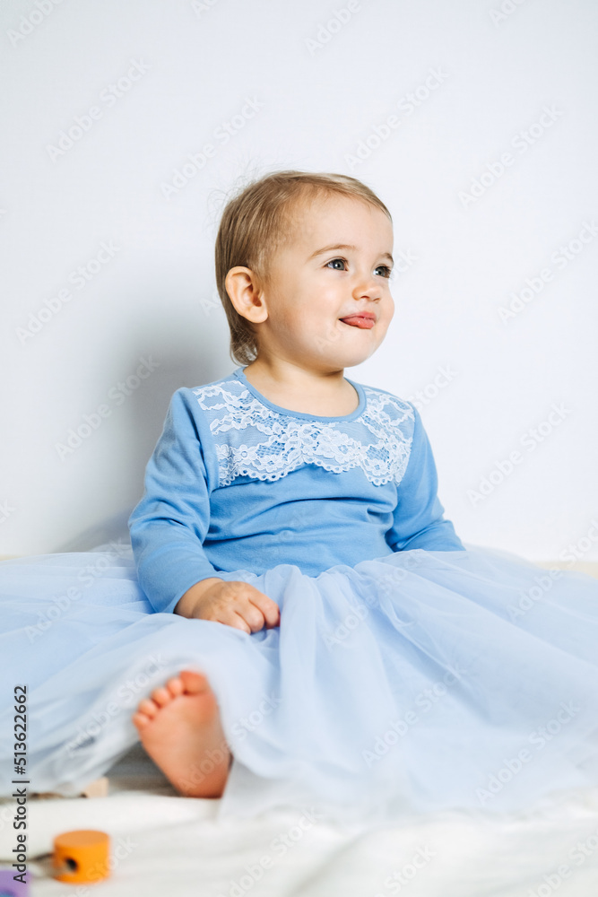 Cute baby girl in blue princess dress playing with toys at home. Kids dresses for prom and birthday holiday Cute baby girl in blue princess dress playing with toys at home. Kids dresses for prom and birthday holiday