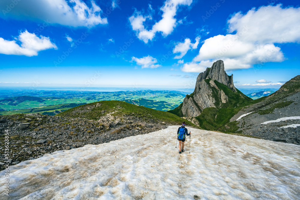 Fototapeta premium Hiker walking accross a snow field with the view on Appenzell and the lake constance