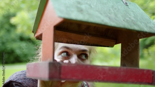 Funny woman looks into bird feeder in park and tries to eat bird food. concept of hunger and need for food, funny. hungry lady grabs bird feeder with her hand and is about to eat all grains and nuts photo