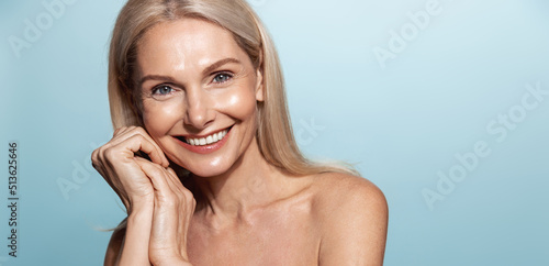 Elegant middle aged woman, head and shoulders with glowing skin, nourished, moisturized face and body, smiling at camera, blue background photo