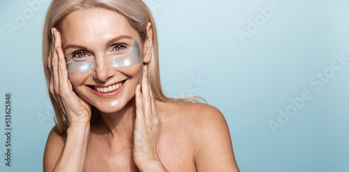Skin care and spa. Beautiful middle aged woman with under eye patches, nourished, glowing skin without aging signs, smiling at camera, blue background