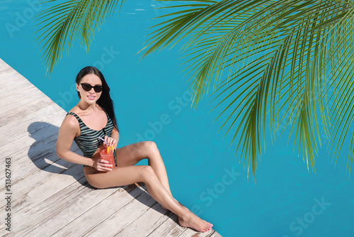 View of beautiful green tropical leaves and young woman with refreshing cocktail near swimming pool on sunny day, above view