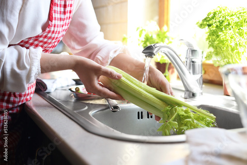 Woman washing fresh celery in kitchen sink, closeup photo