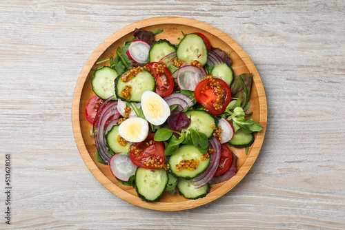Tasty salad with vegetables and quail eggs on wooden table, top view