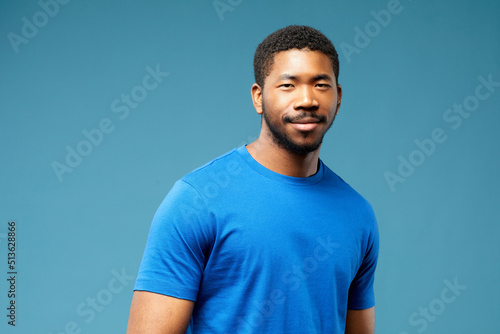 Photo realistic digital collage of smiling multiethnic man with generated artificial face standing against blue background and looking at camera