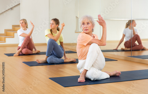 Senior woman practicing lord of fishes pose with her daughter and granddaughter during yoga training in studio.