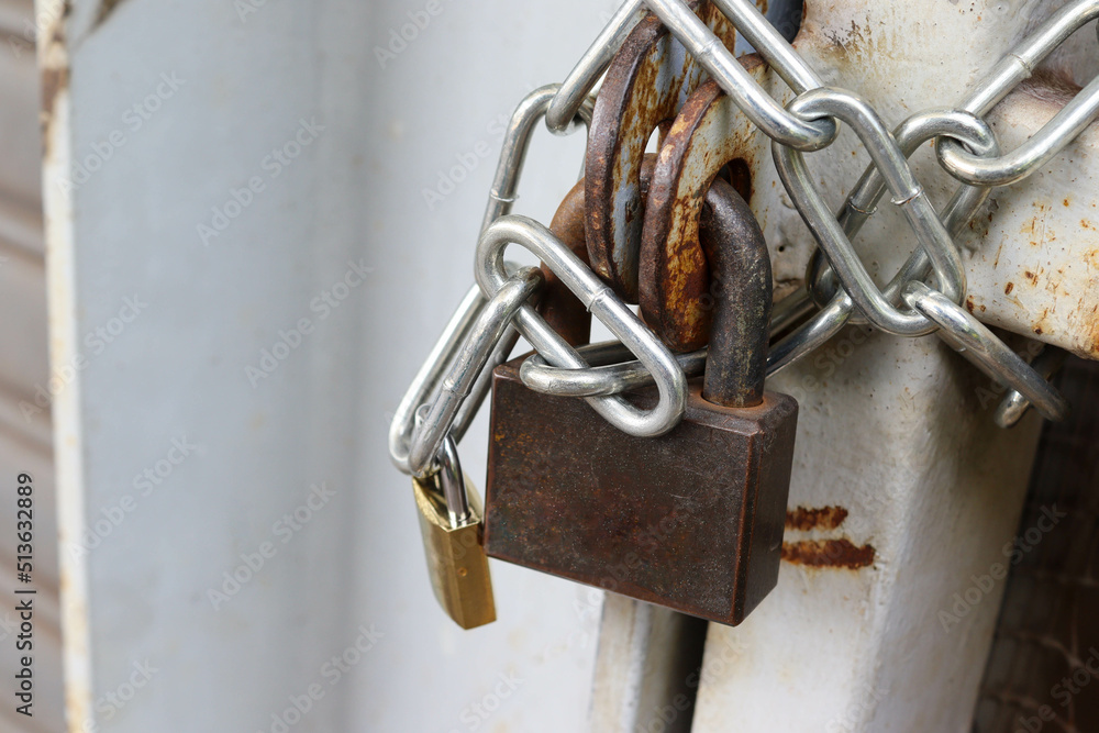 Metal padlock tied to steel chain on rusty iron door closeup.