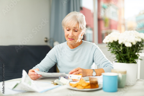 Senior woman counting her budget and checking bills while sitting at table.