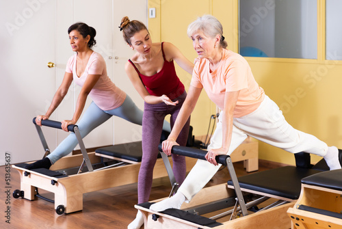 Friendly young girl professional pilates instructor assisting elderly woman to do exercises on reformer. Active lifestyle concept