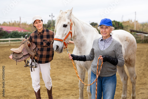 Two positive women preparing a horse for riding in paddock © JackF