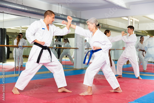 Portrait of concentrated aged woman wearing white kimono sparring with male opponent during martial arts training in gym