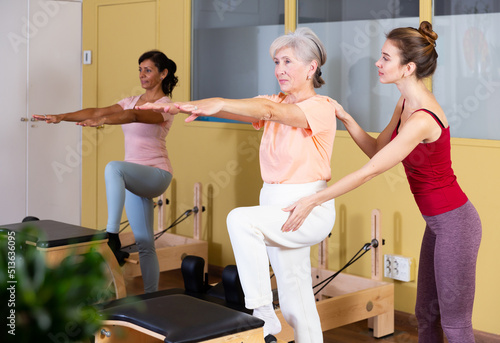Two active women who care about their health perform exercises with outstretched arms during Pilates training with an ..instructor