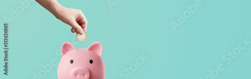 man depositing coins in a pink piggy bank on a blue background - savings concept