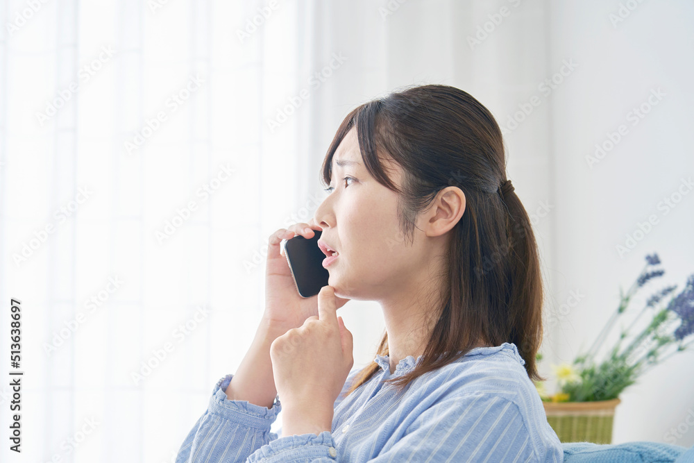 リビングでスマホで電話しながら考える女性 リビングでスマホで電話しながら考える女性