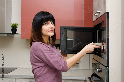 A young woman looks at the camera and takes out a plate from the microwave.