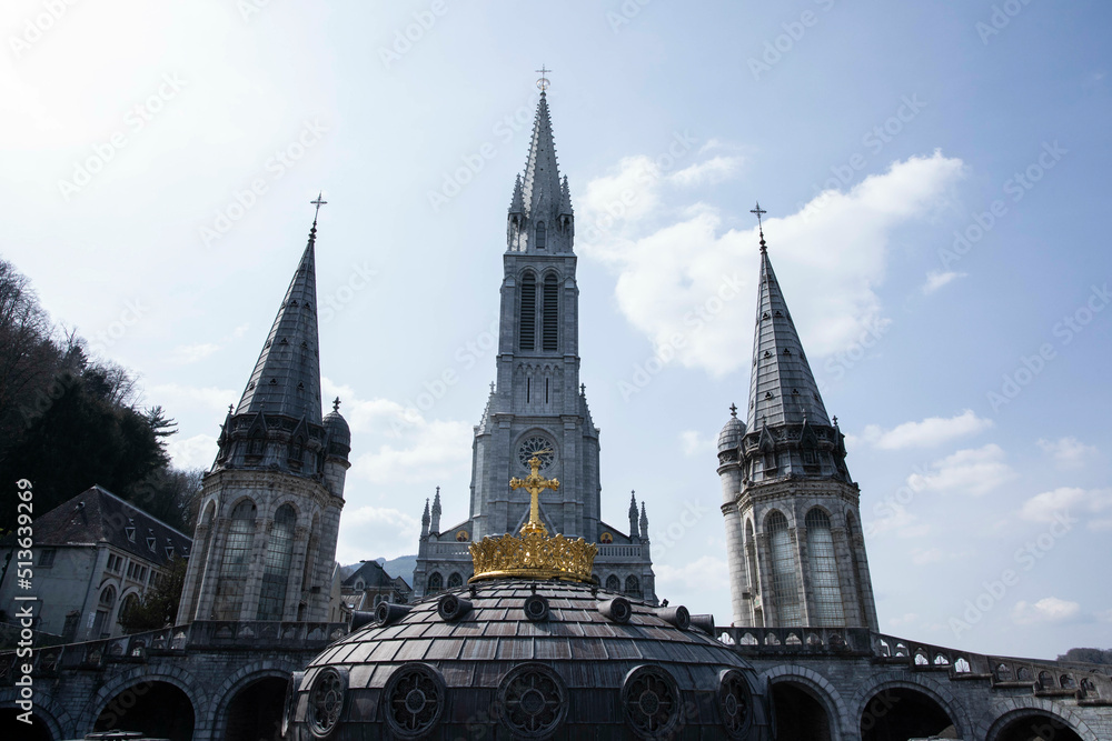 The Gold crown and cross in front of the 3 towers belonging to The Sanctuary of Our Lady of Lourdes in Southern France, Europe The Gold crown and cross in front of the 3 towers belonging to The Sanctuary of Our Lady of Lourdes in Southern France, Europe