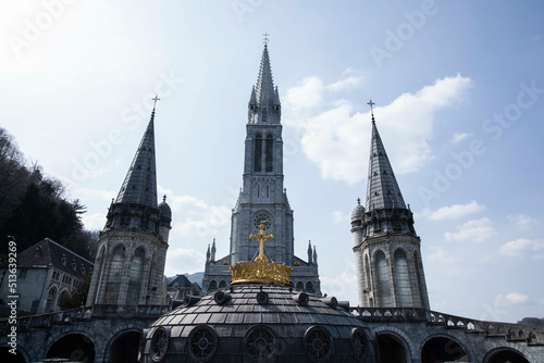 The Gold crown and cross in front of the 3 towers belonging to The Sanctuary of Our Lady of Lourdes in Southern France, Europe