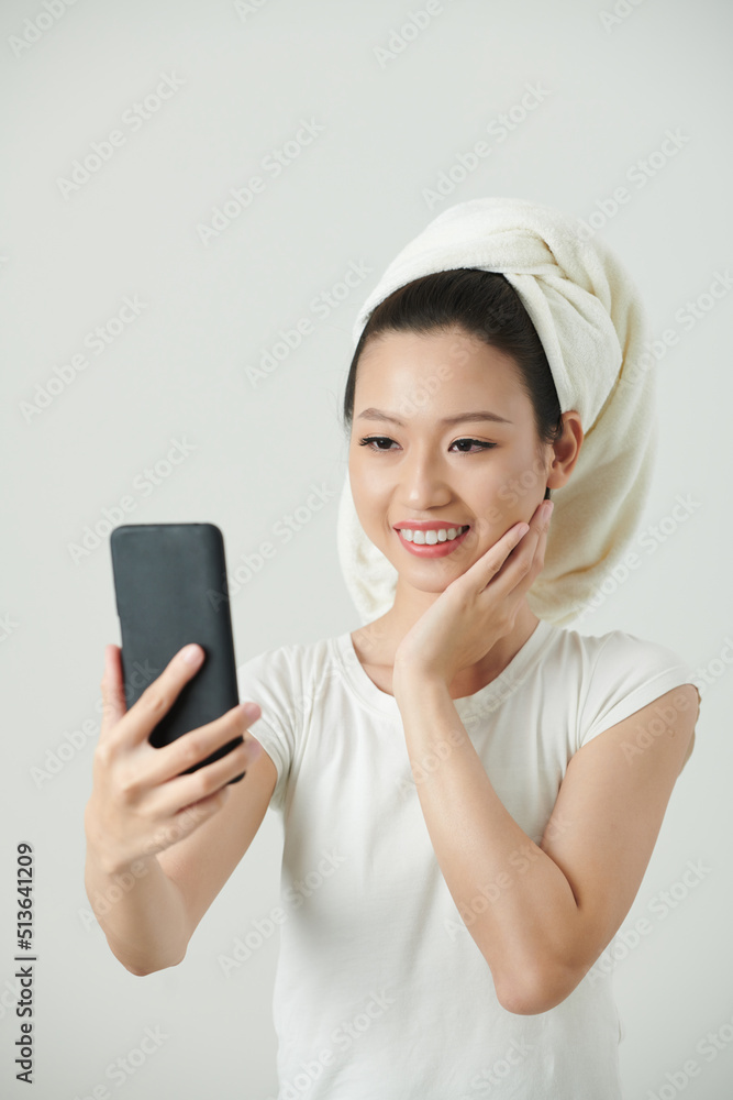 Young Vietnamese woman wtih glowy skin taking selfie on smartphone after shower Young Vietnamese woman wtih glowy skin taking selfie on smartphone after shower