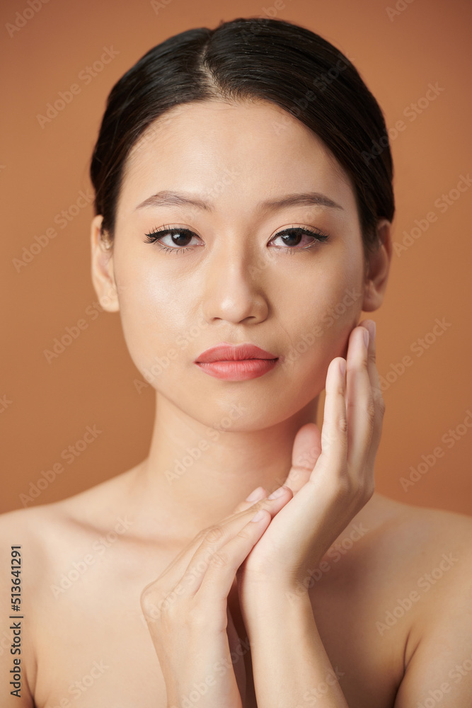 Portrait of serious young woman with natual make-up touching face and looking at camera Portrait of serious young woman with natual make-up touching face and looking at camera