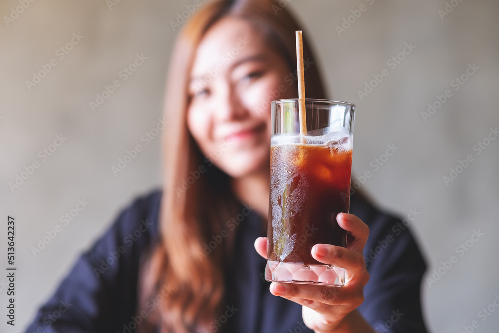 A beautiful young asian woman holding and serving a glass of iced coffee A beautiful young asian woman holding and serving a glass of iced coffee