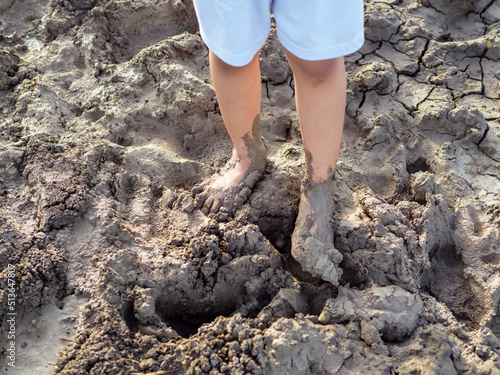 Dirty bare foot child with mud in nature background. Kid playing in mud pit outdoor. Concept of learning nature, fun freedom playing, family activity outdoor, ef learning, skin health care.