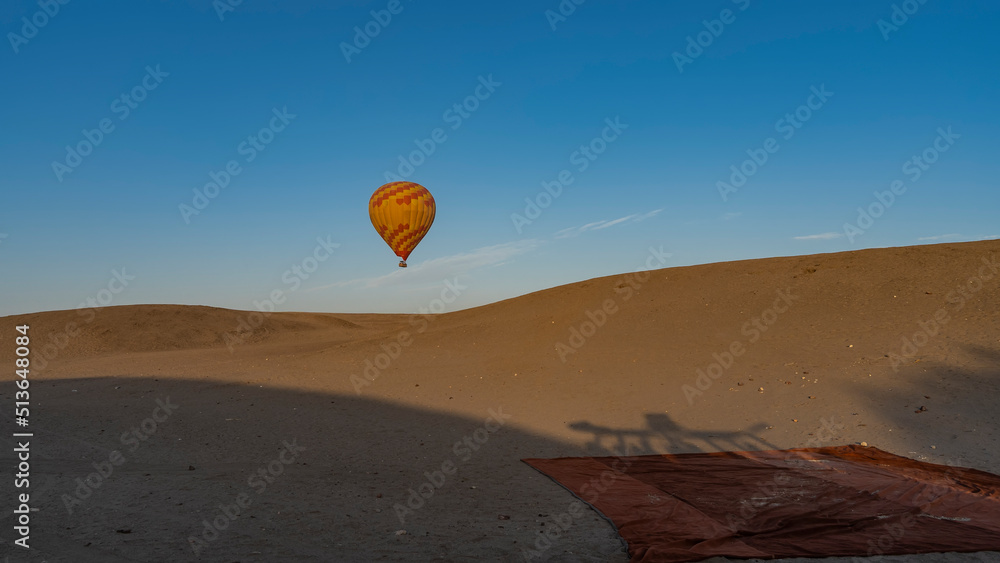 A yellow-red balloon is flying in a clear blue sky over the desert. A carpet is spread out on the sand. light and shadows. Egypt. Luxor