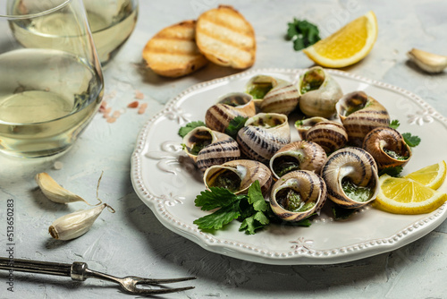Fried snails Escargots de Bourgogne with herbs, butter, garlic on metal plate with forks, wine glass. gourmet food. Restaurant menu, dieting, cookbook recipe
