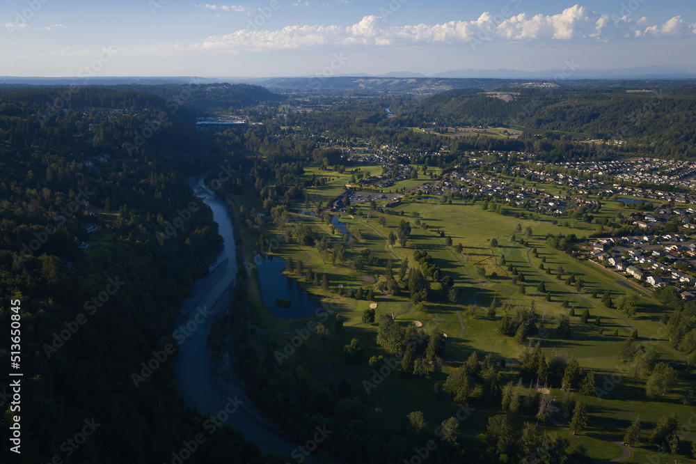 Aerial view of the Puyallup river flowing through a valley with residential houses in the distance.