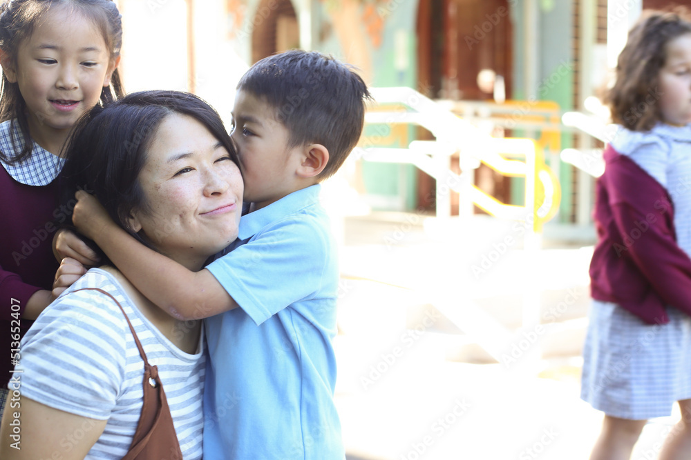 Young boy in school uniform hugging his mum while his sister looks on Young boy in school uniform hugging his mum while his sister looks on