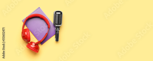 Headphones with microphone and notebook on yellow background with space for text