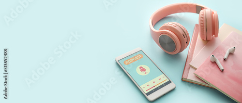 Mobile phone with open podcast playlist, headphones, notebooks and earphones on blue background with space for text photo