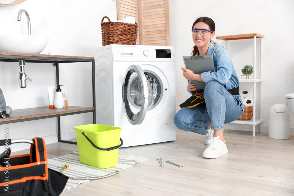 Obraz premium Asian female plumber with clipboard near washing machine in bathroom