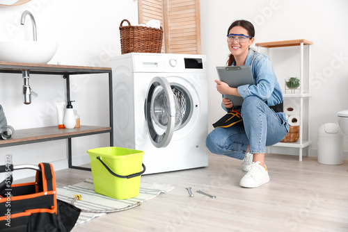 Asian female plumber with clipboard near washing machine in bathroom