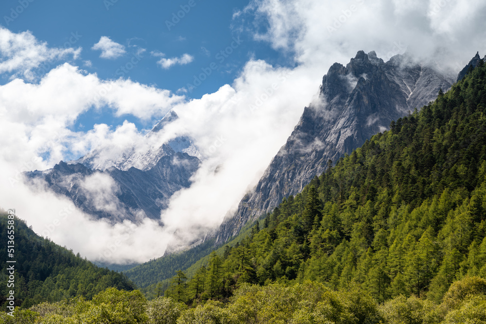Horizontal close up image of the mountains in Daocheng Yading Nature Reserve in dense white clouds, blue sky with copy space for text, background, wallpaper