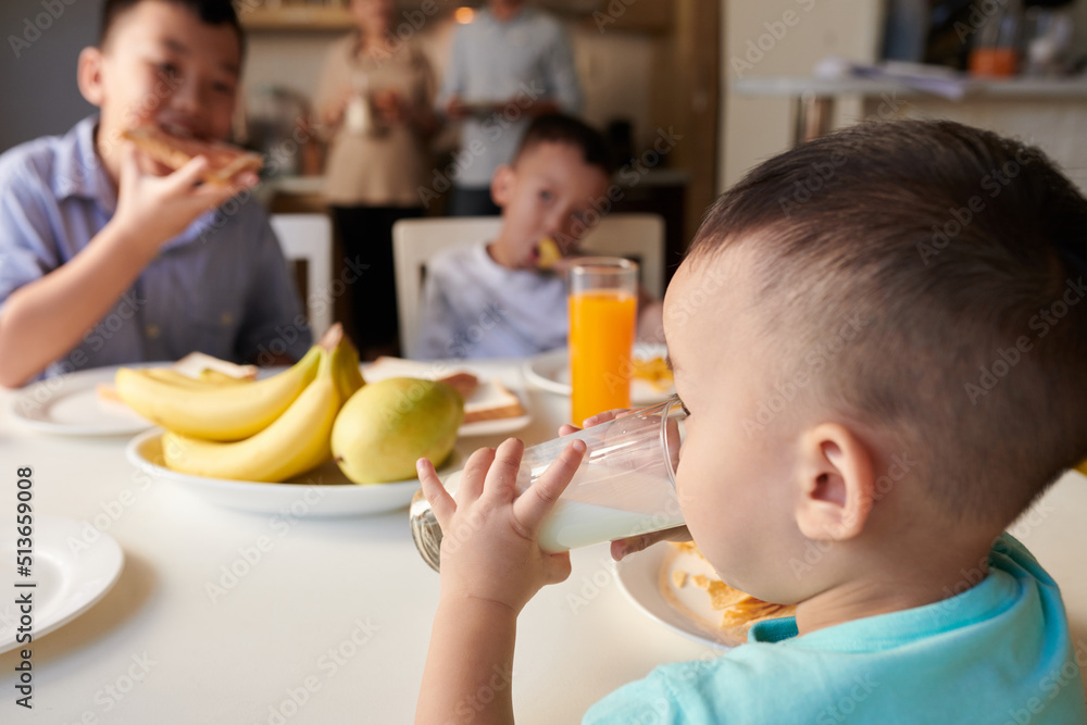 Little boy drinking glass of milk at breakfast table