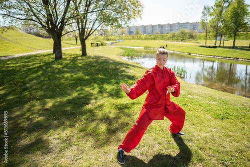 Asian woman in red kimano practicing taijiquan outdoors, chinese martial arts, healthy lifestyle concept. © Pavel