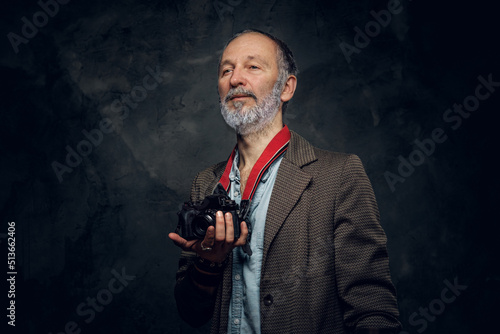 Shot of stylish elderly man photographer with photocamera against dark background.