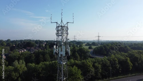 5G broadcasting tower antenna in British countryside woodland with vehicles travelling on highway background rising aerial view