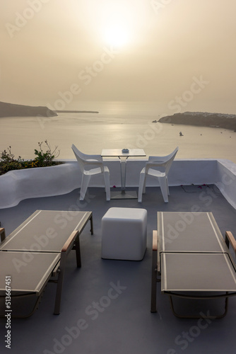Sun loungers and chairs on terrace in the village of Imerovigli with amazing view of sunset over caldera in Santorini, Greece © wjarek