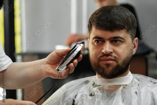 Barber guy gives a haircut to a bearded man sitting in a chair in a barbershop