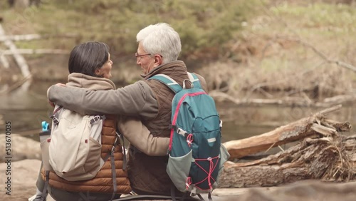Wallpaper Mural Rear view slowmo of mature active couple with hiking backpacks sitting by lake in forest embracing each other and enjoying nature Torontodigital.ca