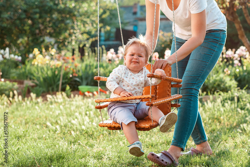 Preschool education. A young mother rides a capricious toddler on a swing. Family games on the sunny playground in the park. The concept of the International Children's Day
