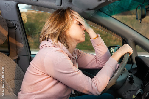 A young blonde nervous woman is sitting behind the wheel of a left-hand drive car and holding her head. Side view. Fine for violation of traffic rules photo