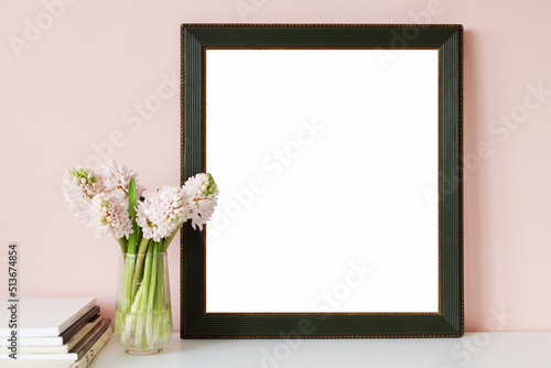 Minimalistic indoor image of cozy interior objects against pink wall background. Pink hyacinths flowers in nice jar and empty vintage rectangular photo frame for your picture, design or painting