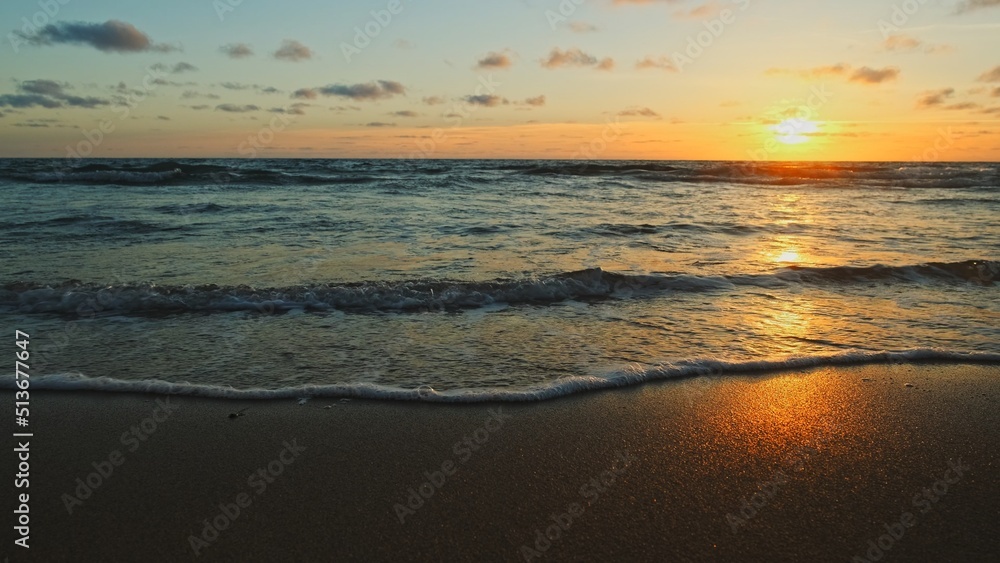 Beautiful sandy beach while sunset. Beautiful seascape of a sandy beach. Sun over horizon and  rolling ocean waves to the shore while sunset. Summer, travel and tourism. Beautiful wild nature.