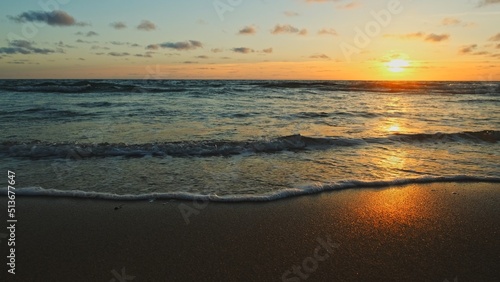 Beautiful sandy beach while sunset. Beautiful seascape of a sandy beach. Sun over horizon and  rolling ocean waves to the shore while sunset. Summer  travel and tourism. Beautiful wild nature.